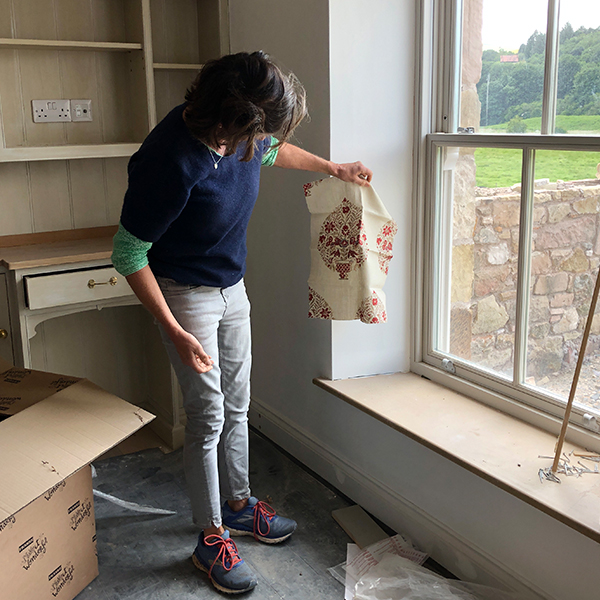 Corinne standing by the kitchen window in Housedon Haugh looking at a curtain sample