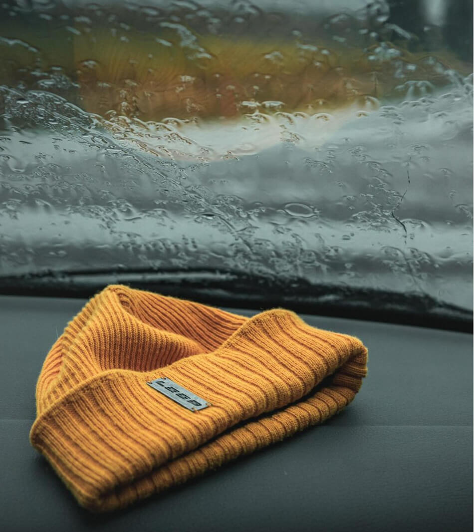 Loop orange beanie sitting on the dashboard of a car with rain pouring down the window