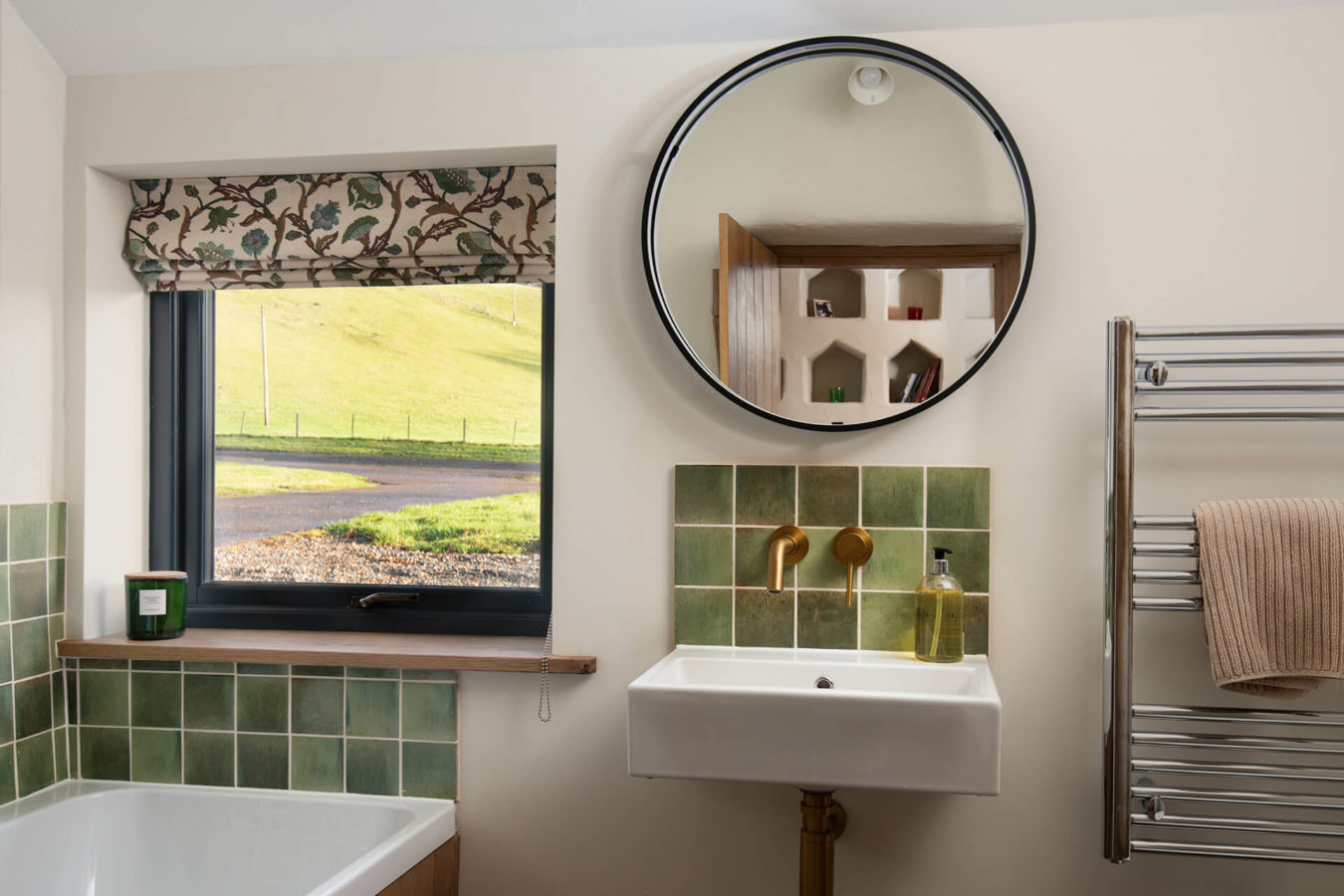 Bathroom in The Dovecot at Reedsford with green tiles large round mirror with view back over the nesting boxes and window looking out over the river